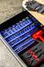 Open tool box drawer with organized socket set and tools with mechanic gloves on the tool bench
